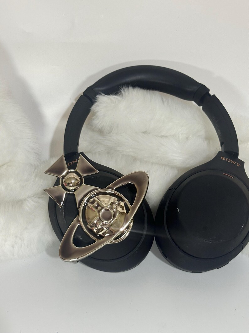 May include: Black Sony headphones with a silver decorative emblem. The headphones have a padded headband and earcups. The emblem is a silver-colored design with a planet-like shape.