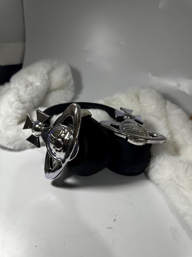 May include: A pair of black headphones with silver orb-shaped accents. The headphones have a black headband and earcups. The orb accents are detailed with a star and a circle.