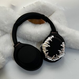 May include: Black over-ear headphones with a silver, sharp, tooth-like design on one earcup. The headphones have the word "SONY" printed on both earcups.