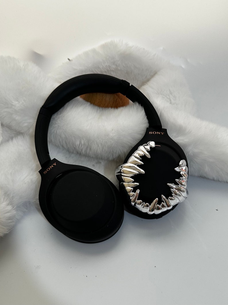 May include: Black over-ear headphones with a silver, sharp, tooth-like design on one earcup. The headphones have the word "SONY" printed on both earcups.
