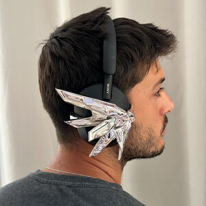 Puede incluir: Auriculares Sony negros con un dise&ntilde;o geom&eacute;trico plateado fijado a la orejera. Los auriculares los lleva una persona con una camiseta gris. El logotipo de Sony es visible en el lateral de los auriculares.