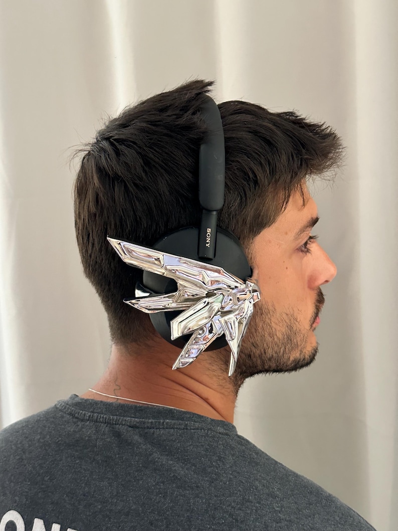 Puede incluir: Auriculares Sony negros con un dise&ntilde;o geom&eacute;trico plateado fijado a la orejera. Los auriculares los lleva una persona con una camiseta gris. El logotipo de Sony es visible en el lateral de los auriculares.