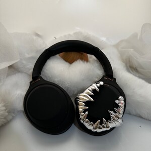 May include: Black wireless headphones with a silver, toothy, monster-like design on one earcup. The headphones have the word "SONY" printed on the side.