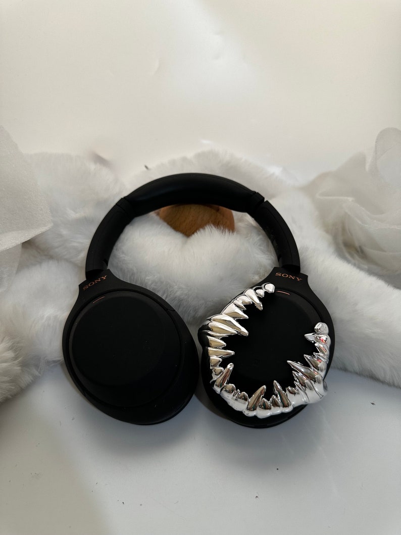 May include: Black wireless headphones with a silver, toothy, monster-like design on one earcup. The headphones have the word "SONY" printed on the side.