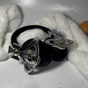 May include: Black headphones with silver orb-shaped accents. The orbs have a cross design and a small orb in the centre.