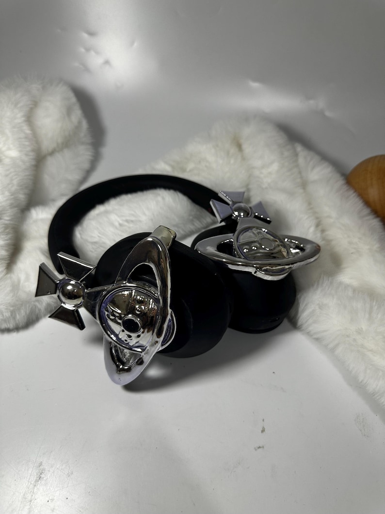 May include: Black headphones with silver orb-shaped accents. The orbs have a cross design and a small orb in the centre.