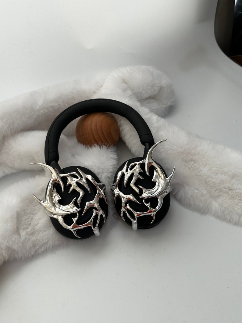May include: Black headphones with silver decorative accents in the shape of a stylized flame design.