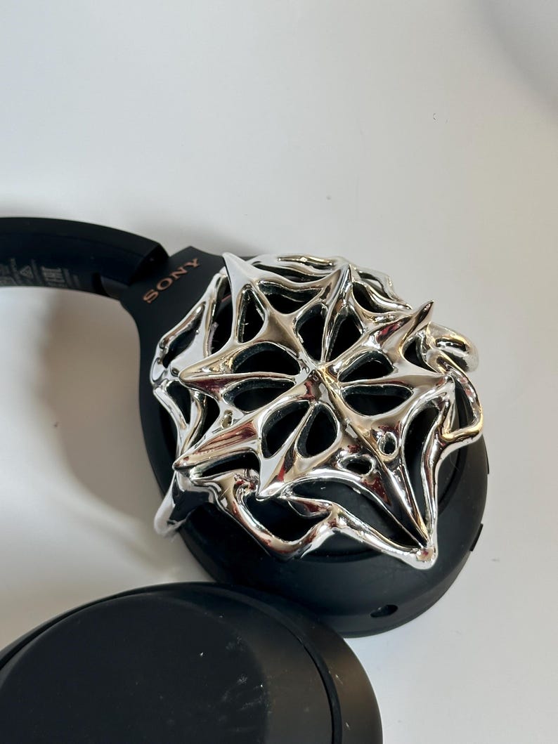 May include: Black Sony headphones with a silver, star-shaped decorative accent. The headphones are on a white surface. The word "SONY" is visible on the side of the headphones.