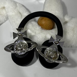 May include: Black headphones with silver orb and cross accents. The orb features a circular design with a smaller circle in the centre.