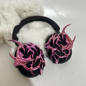 May include: Pink and black headphones with a decorative, metallic, flame-like design on the earcups.