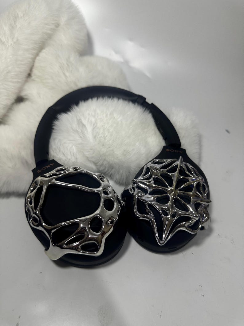 May include: Black over-ear headphones with silver decorative accents. The headphones have a black headband and earcups, with intricate silver designs on the earcups. The Sony logo is visible on the headphones.