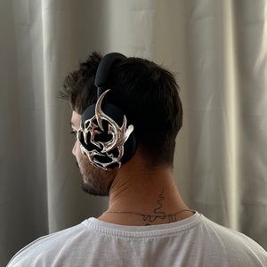 May include: A person wearing black headphones with a silver, decorative,  ornate design on the side.
