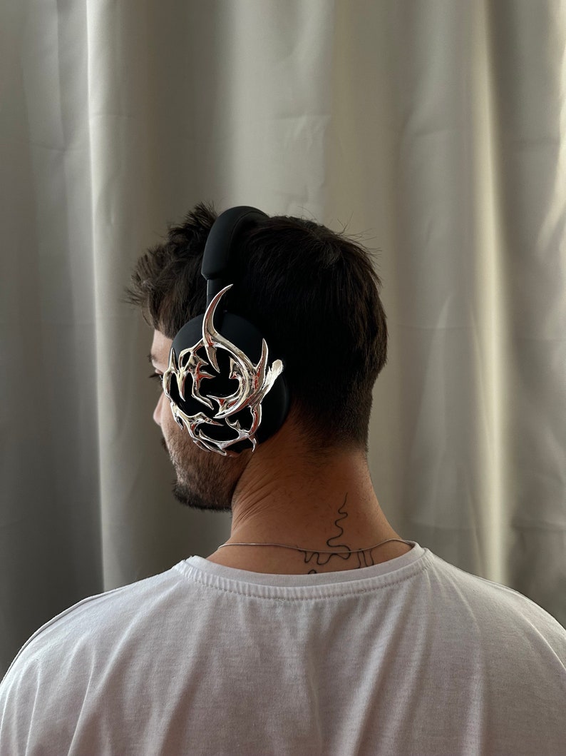 May include: A person wearing black headphones with a silver, decorative,  ornate design on the side.
