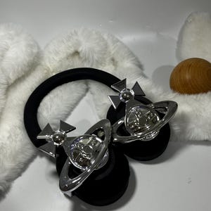 May include: Black headphones with silver orb and cross accents. The headphones have a black headband and earcups.