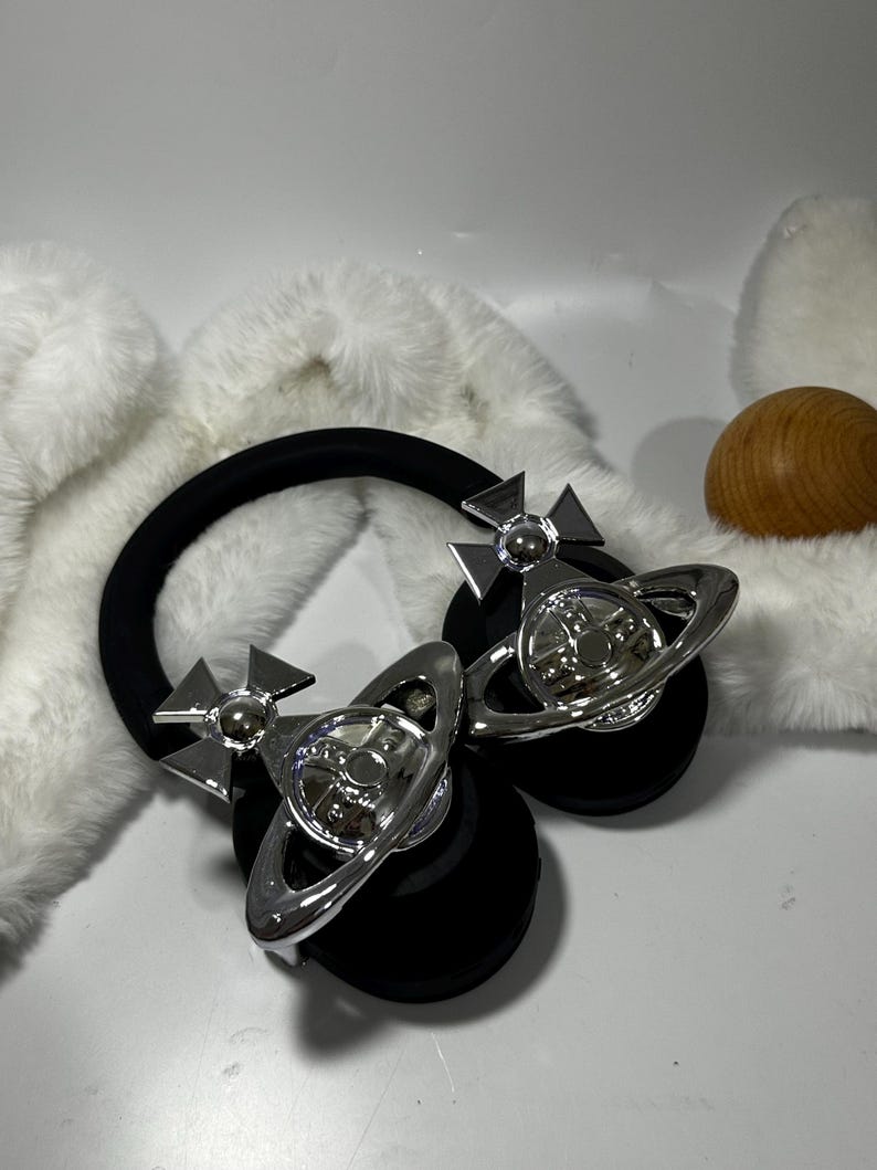 May include: Black headphones with silver orb and cross accents. The headphones have a black headband and earcups.