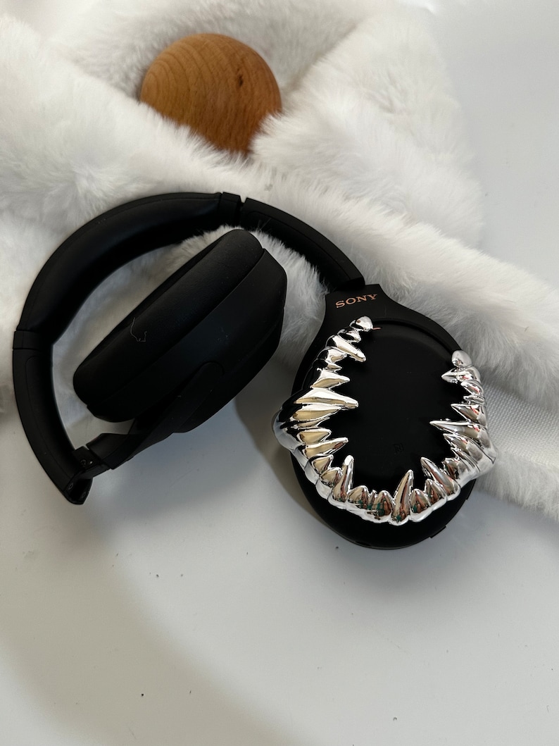May include: Black wireless headphones with a silver, sharp, tooth-like design on the earcup. The text "SONY" is printed in pink on the earcup.