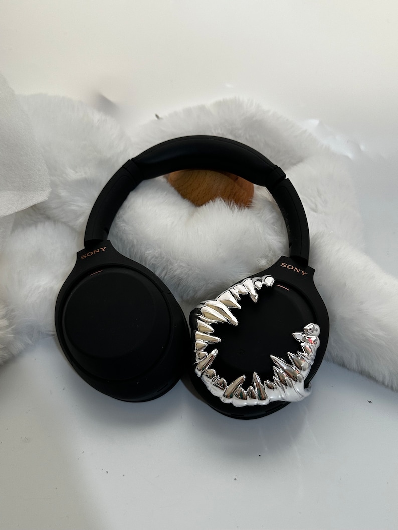 May include: Black wireless headphones with a silver, toothy, monster-like design on one earcup. The headphones have the word "SONY" printed on both earcups.