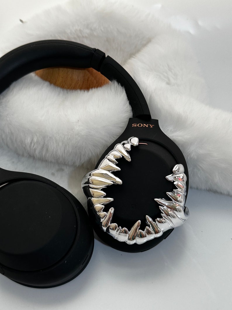May include: Black wireless headphones with a silver, sharp, tooth-like design on the earcup. The headphones have the word "SONY" printed on the earcup.