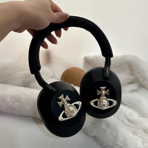 Puede incluir: Auriculares negros de diadema con detalles plateados. Los auriculares tienen una diadema y almohadillas acolchadas. Los auriculares presentan un dise&ntilde;o plateado de orbe y cruz. La marca "SONY" es visible en el lateral de los auriculares.