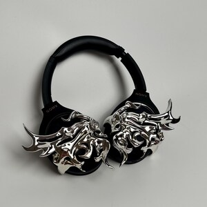May include: Black Sony headphones with silver, flame-like embellishments on the earcups. The headphones have a padded headband and earcups for comfort. The silver accents add a unique, artistic flair to the headphones.