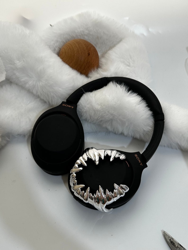 May include: Black wireless headphones with a silver, fang-like design on one earcup. The headphones have the word "SONY" printed on the earcup.