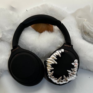 May include: Black wireless headphones with a silver, sharp teeth design on one earcup. The headphones have the word "SONY" printed on the side.