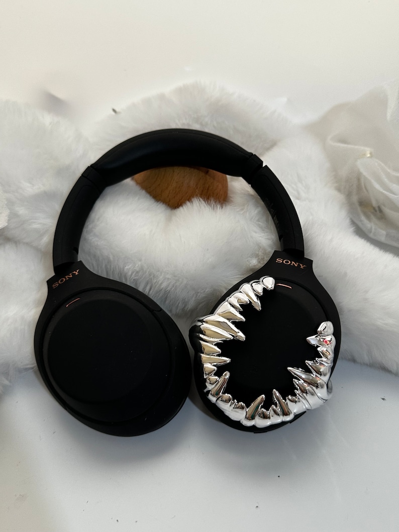 May include: Black wireless headphones with a silver, sharp teeth design on one earcup. The headphones have the word "SONY" printed on the side.