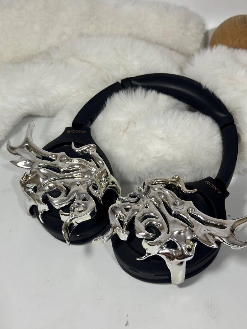 May include: Black over-ear headphones with silver flame-like embellishments. The headphones have the brand name "SONY" printed on the side. The background is a white surface with a fluffy white texture.