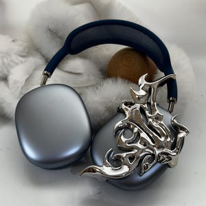 May include: A pair of silver headphones with a blue headband and a silver, flame-like design on the earcups.