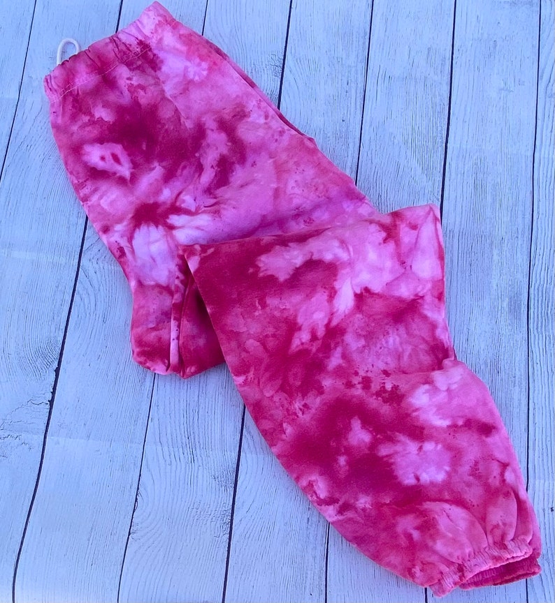 May include: Pink tie-dye sweatpants with a white background. The sweatpants are made of a soft, comfortable fabric.