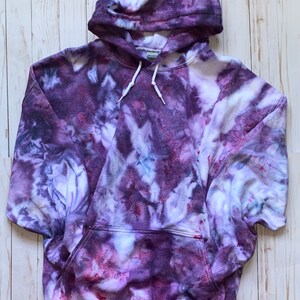 May include: Purple tie-dye hoodie with a white drawstring and a kangaroo pocket.
