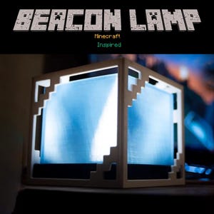 Può includere: Una lampada a cubo bianca e pixelata con un interno blu brillante. La lampada è ispirata al videogioco Minecraft. Il testo "BEACON LAMP" è sopra la lampada, con "Minecraft Inspired" sotto.