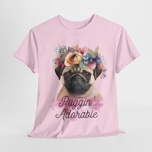 May include: A pink t-shirt with a floral crown and a pug wearing the crown. The text "Puggin' Adorable" is printed on the shirt.