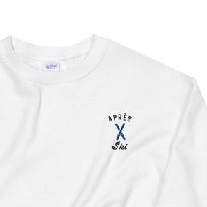 Puede incluir: Sudadera blanca con un logotipo bordado en azul y negro que dice "Apr&egrave;s Ski" con un par de esqu&iacute;s cruzados.
