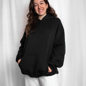 May include: A person wearing a black oversized hoodie with a hood and white trousers.
