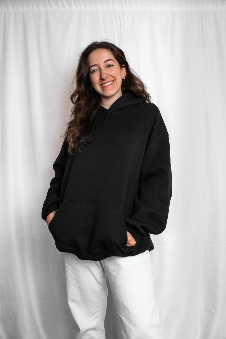 May include: A person wearing a black oversized hoodie with a hood and white trousers.