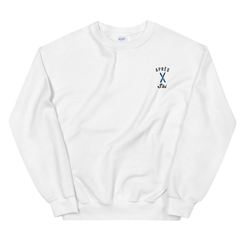 Puede incluir: Sudadera blanca con un logotipo bordado en azul y negro que dice "Apr&egrave;s Ski" con un par de esqu&iacute;s cruzados.