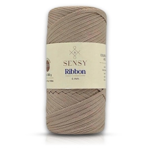 Könnte beinhalten: Ein Knäuel beigefarbenes Sensy Ribbon Garn, ein 4 mm dickes Bandgarn, mit dem Markennamen und der Größe auf dem Etikett.