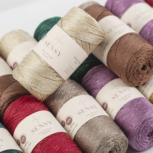 Peut inclure: Gros plan sur une vari&eacute;t&eacute; de bobines color&eacute;es de cordon PP de 2 mm avec des paillettes. Les bobines sont dispos&eacute;es en demi-cercle, avec la bobine dor&eacute;e au centre. Les bobines sont &eacute;tiquet&eacute;es avec le nom de la marque "SENSY" et le texte "Cordon PP 2 mm Paillettes".