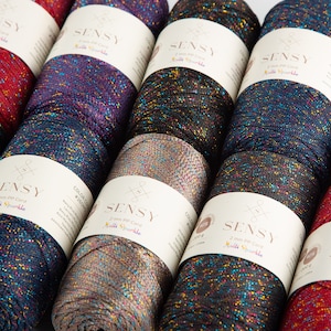Puede incluir: Primer plano de diez carretes de hilo de colores brillantes. El hilo es un cord&oacute;n PP de 2 mm y est&aacute; etiquetado como "SENSY Multi Sparkle".