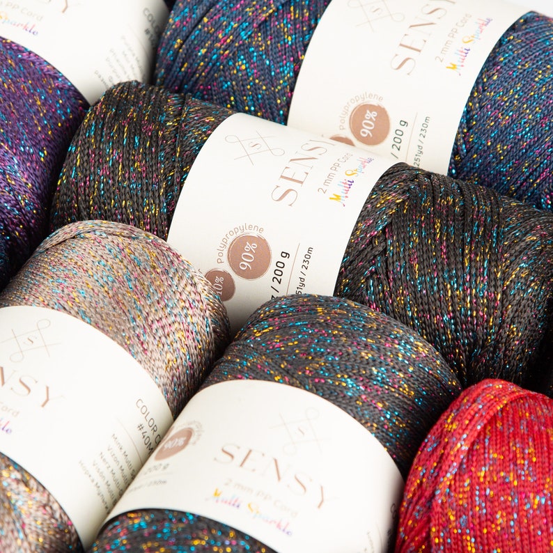 Puede incluir: Primer plano de carretes de hilo de colores con purpurina. El hilo est&aacute; etiquetado como "SENSY" y est&aacute; hecho de 90% polipropileno. Los carretes son de 200 gramos y 230 yardas.