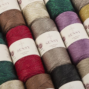 Peut inclure: Gros plan sur des bobines de fil brillant en cordon PP de 2 mm dans diff&eacute;rentes couleurs, notamment rouge, vert, or, marron et violet. Chaque bobine porte une &eacute;tiquette avec le nom de la marque "SENSY" et le texte "2 mm PP Cord Sparkle".