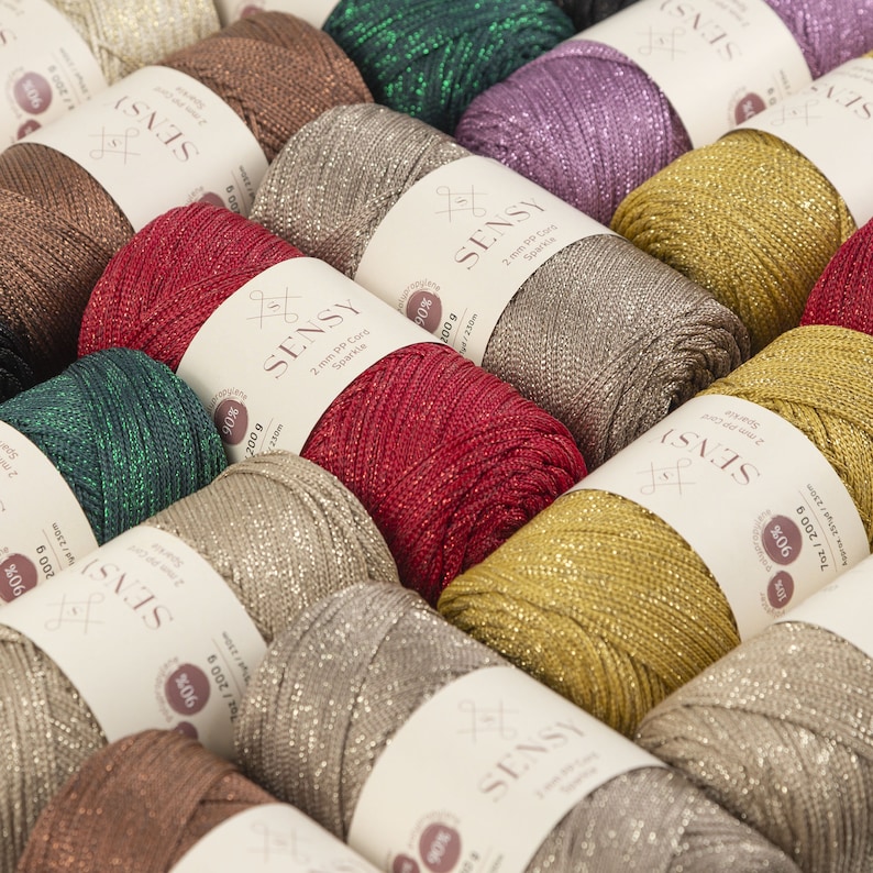 Peut inclure: Une collection de bobines de fil brillant de diff&eacute;rentes couleurs, dont l'or, le rouge, le vert, le marron et l'argent. Le fil est &eacute;tiquet&eacute; "SENSY" et est compos&eacute; de 90% de polyester et de 10% de m&eacute;tal.