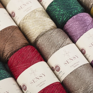 Peut inclure: Gros plan sur des bobines de cordon paillet&eacute; de diff&eacute;rentes couleurs, dont l'or, le vert, le violet, le marron et le rouge. Les bobines sont &eacute;tiquet&eacute;es "SENSY 2 mm PP Cord Sparkle 90% Polypropyl&egrave;ne 200 g 25/230m".