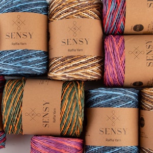May include: Assortment of colorful raffia yarn spools with brown labels that read "SENSY Raffia Yarn".