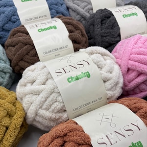 Puede incluir: Surtido de ovillos de lana de colores etiquetados como "SENSY Chunky" con c&oacute;digos de color y nombres. La lana es suave y esponjosa, perfecta para tejer al crochet o tejer.