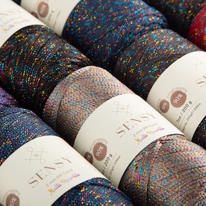 Puede incluir: Primer plano de varios carretes de hilo Sensy 2 mm PP Cord Multi Sparkle. El hilo es una mezcla de 90% polipropileno y 10% poli&eacute;ster y viene en una variedad de colores con un acabado brillante. Cada carrete contiene 200 g (7 oz) de hilo y tiene aproximadamente 230 m (251 yardas) de largo.