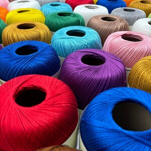 May include: A collection of colorful yarn spools in various shades of blue, red, purple, yellow, and green. The spools are arranged in a circular pattern, creating a vibrant and textured display.