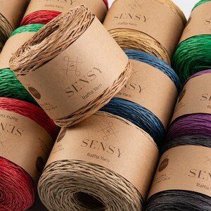 May include: Assortment of colorful raffia yarn spools with the brand name "SENSY" printed on the labels. Each spool is wrapped in a natural brown paper with a white label.