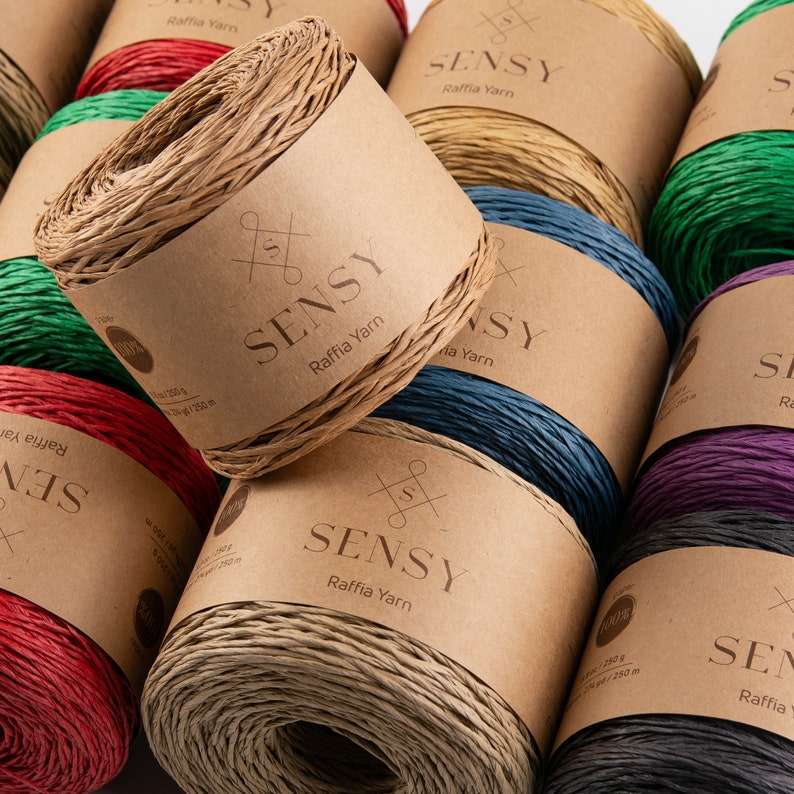 May include: Assortment of colorful raffia yarn spools with the brand name "SENSY" printed on the labels. Each spool is wrapped in a natural brown paper with a white label.